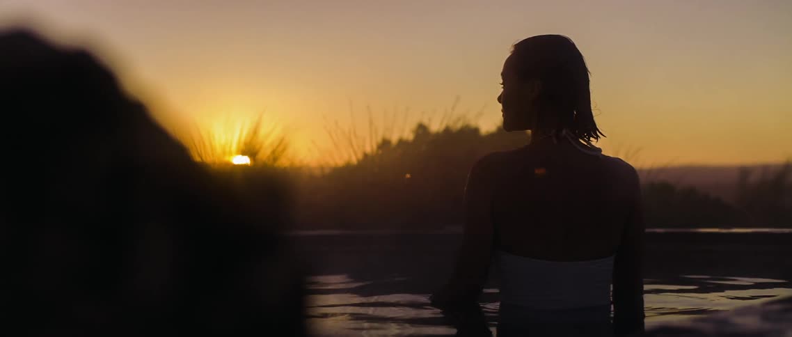 A woman stands in the water as the sunsets in front of her