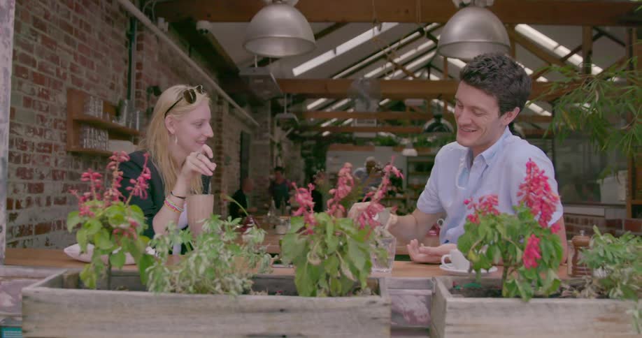 A couple talking and smiling at an outdoor restaurant while the man refills his drink glass