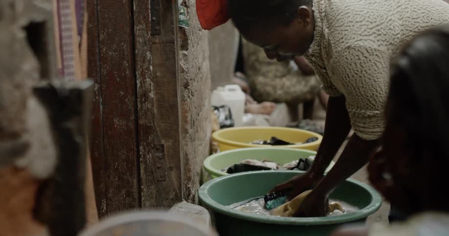 A black woman washing clothing in a plastic tub