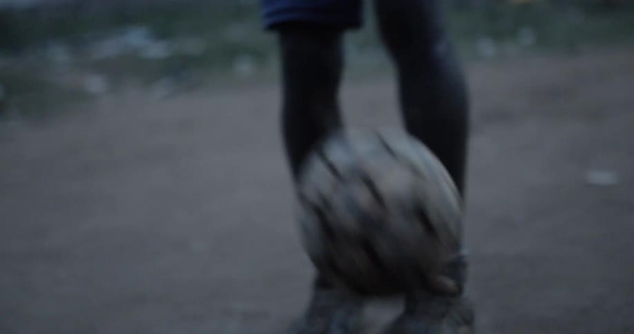A child is kicking a soccer ball on a dirt surface
