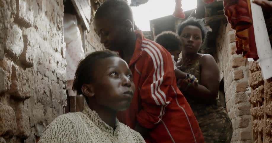 A group of black people talk in a small room with clothes hanging from the ceiling