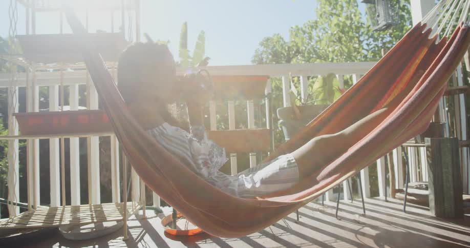 A girl sits in a hammock drinking from a cup