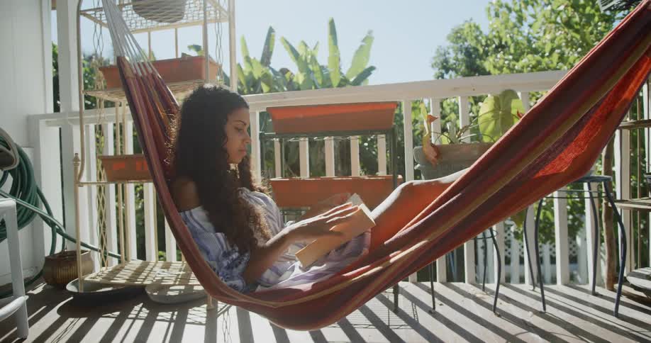 A young woman reading a book while resting in a hammock