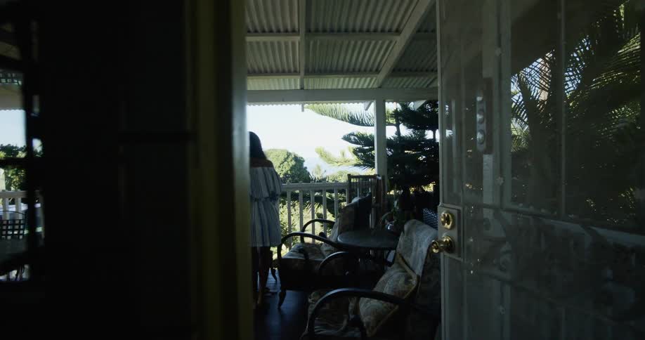 A woman walks through a door and out onto a covered porch to sit down and put her feet up