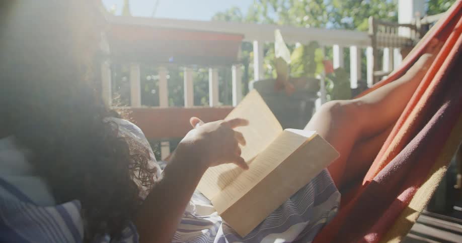 A woman laying on a hammock on a balcony reading a book