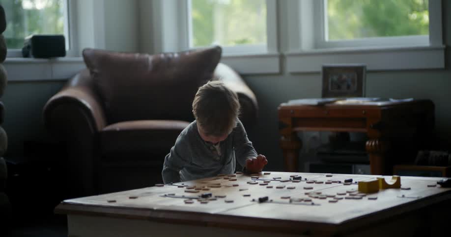 A small child standing at a coffee table is picking up blocks and placing on the tabletop
