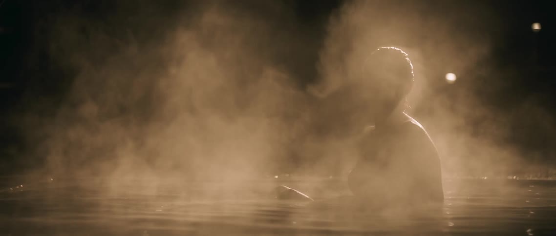 A woman sits up in a shallow pool of steaming water