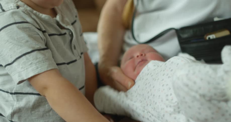 A young boy looks at a baby a woman is holding