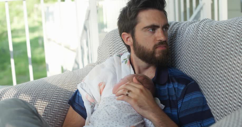 A white man sits in a chair cradling a baby
