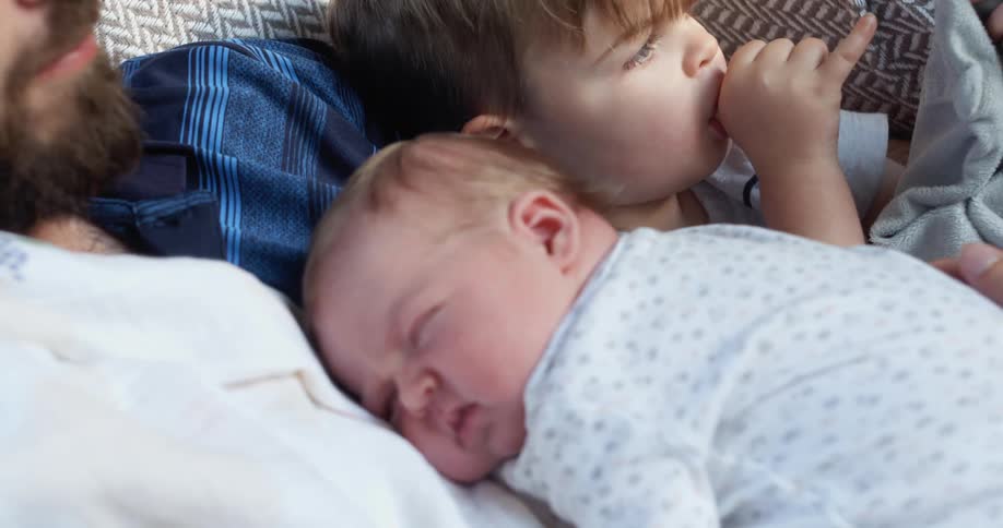 A man sits on the couch with his son beside him and his newborn on his chest