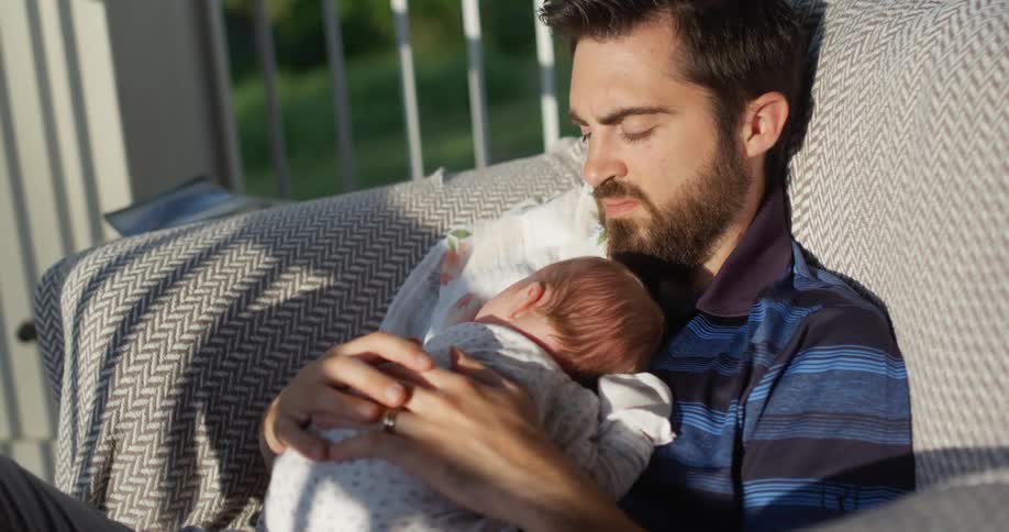 Man sitting on the couch holds infant and caresses outdoors at sunset
