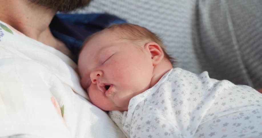 A newborn sleeps with her mouth open on her dads chest