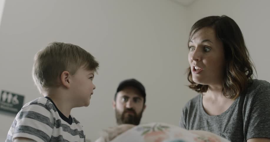 A little boy talks to his mom and looks at his newborn sibling