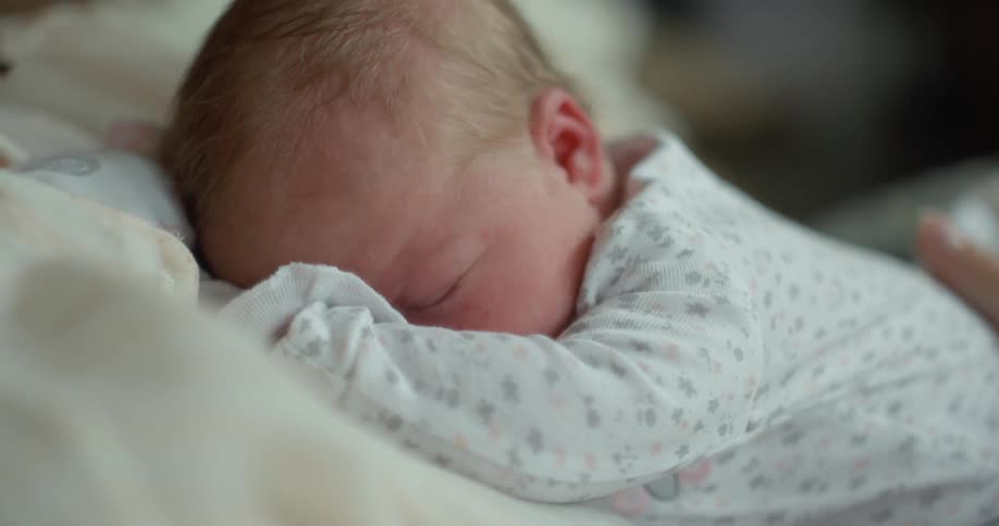 A person stroking a babys head as it sleeps on their chest