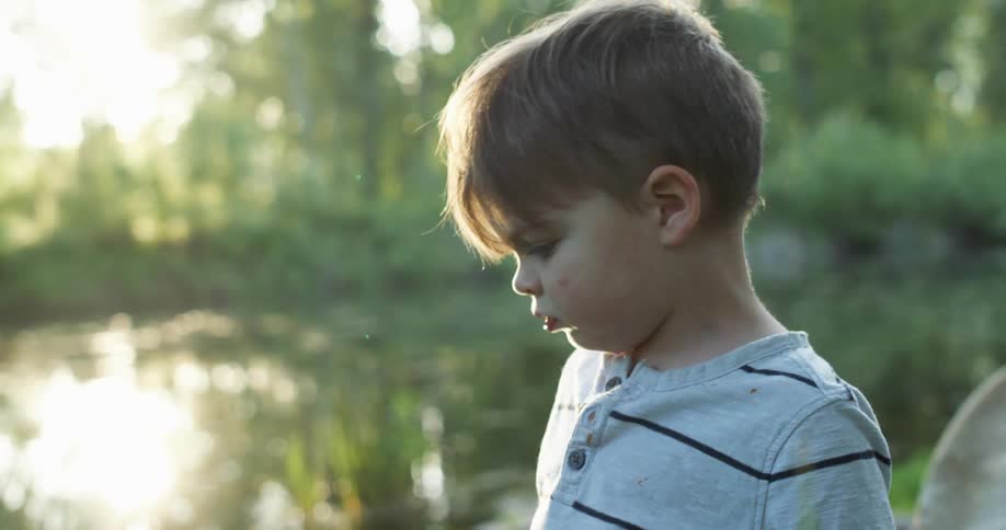 A boy standing and walking by a pond