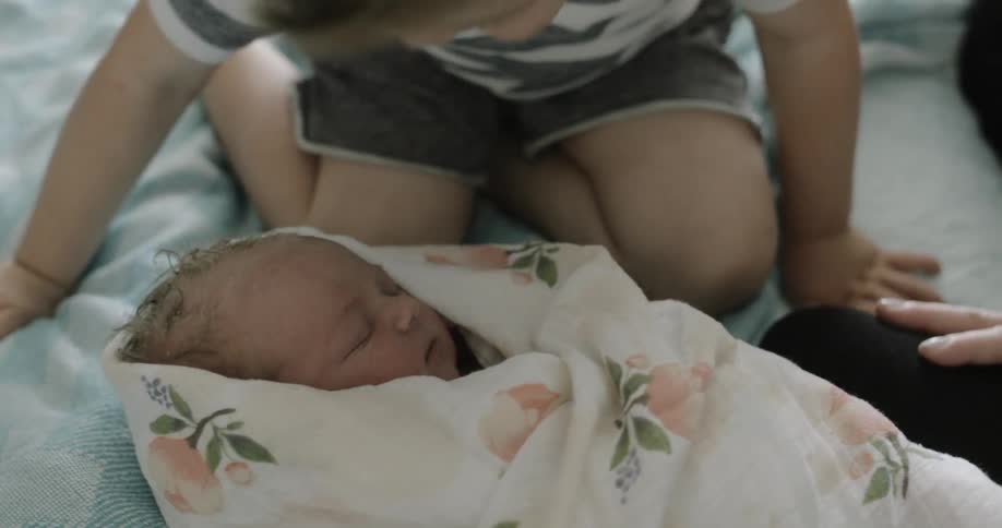 A toddler boy kisses the forehead of their newborn sibling in the hospital
