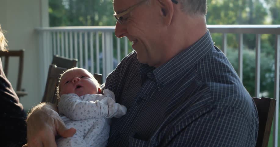 An older white man smiles as he holds a small baby