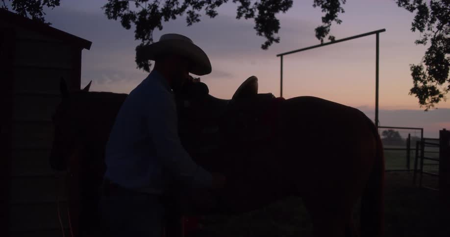 A cowboy adjusts the stirrup on a horse