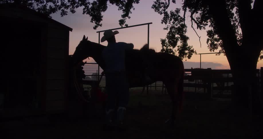 A man with a cowboy hat putting on a saddle on a horse