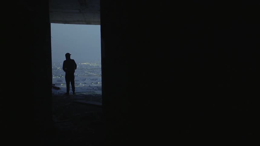 A man stands at the end of a hallway and looks out of a balcony