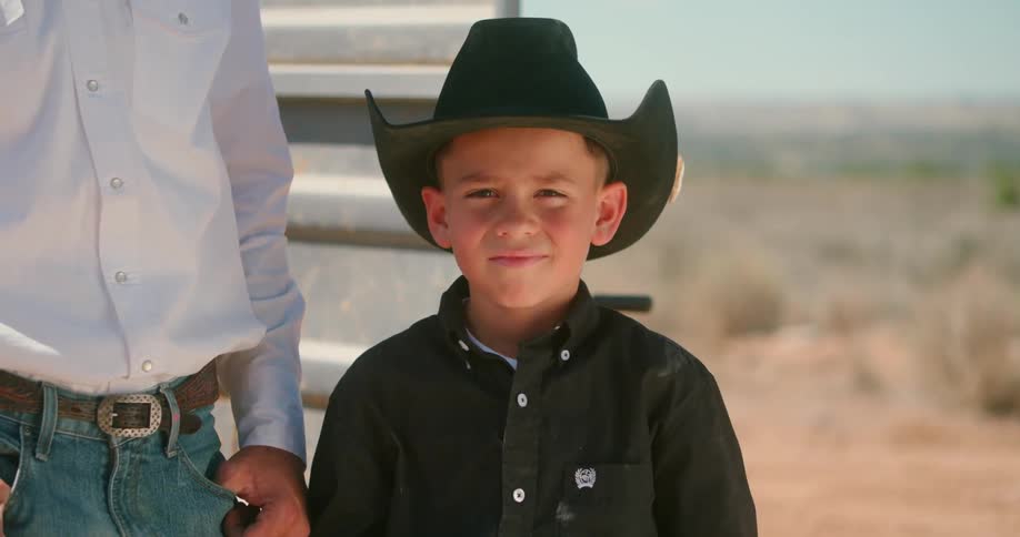 A young boy wearing a cowboy hat stands next to a man outside