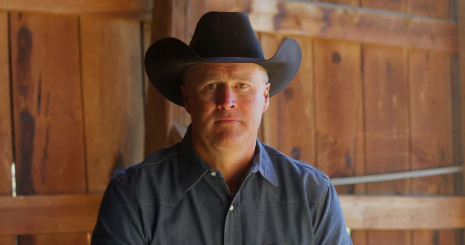 Man wearing a black cowboy hat looks at the camera in the stable