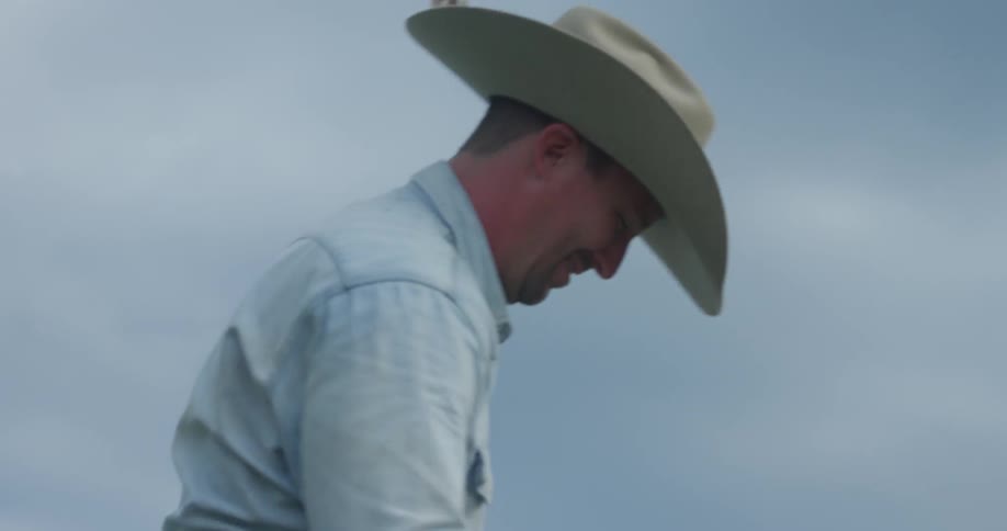 Man wearing a cowboy hat gets on the horse on a cloudy day