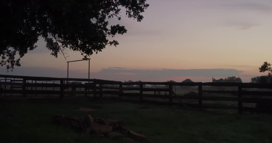 A wood fence surrounds a pasture on a ranch at sunset