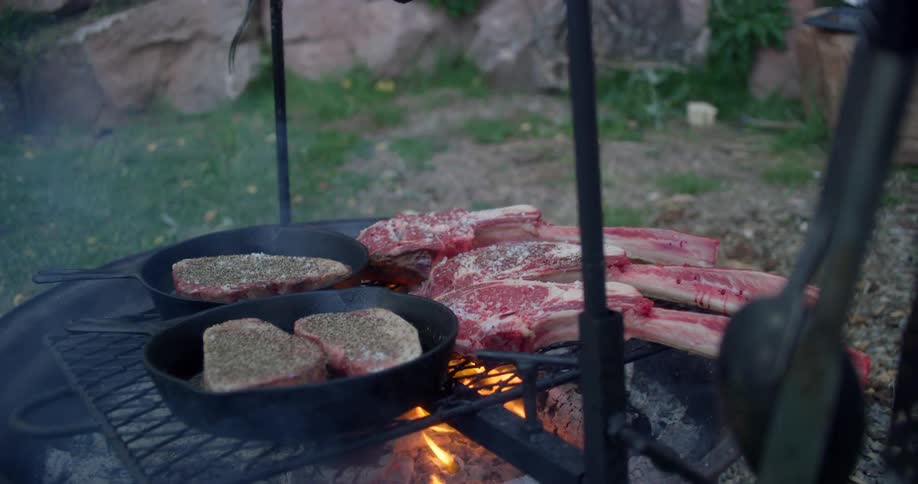 Multiple pieces of seasoned meat cook on an open flame outside