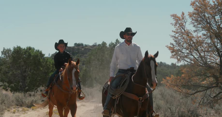 A man and a boy riding horses along a dirt road