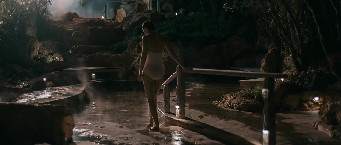 A woman in a full bathing suit walks to a wading pool at night