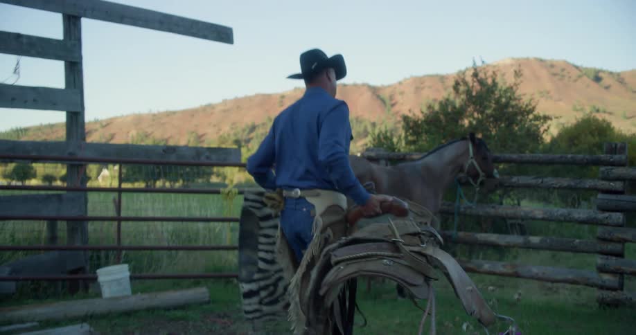 A man carrying a saddle to a horse