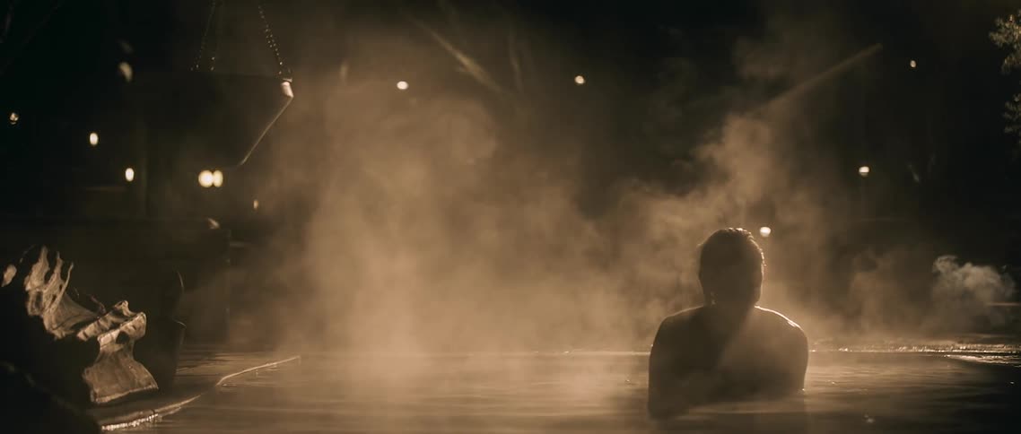 A woman laying in a pool of steaming water sits up and looks around