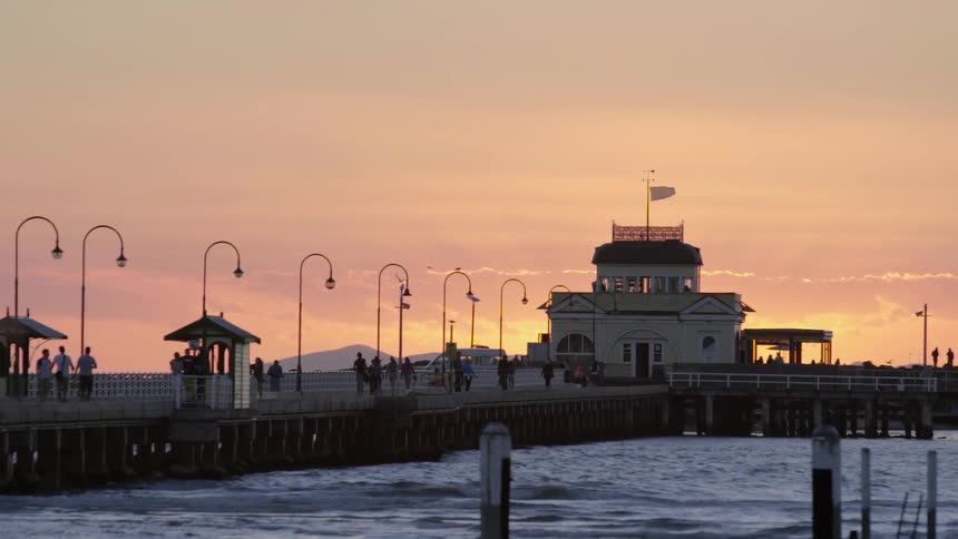 People walking along a long pier with a building located at the end during sunset