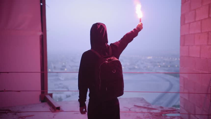 A person standing near the open ledge of a building holds a flare