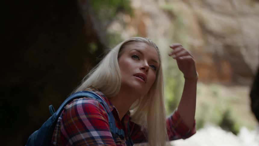 Blonde woman sitting down on a big rock looks around in the stream between two mountains