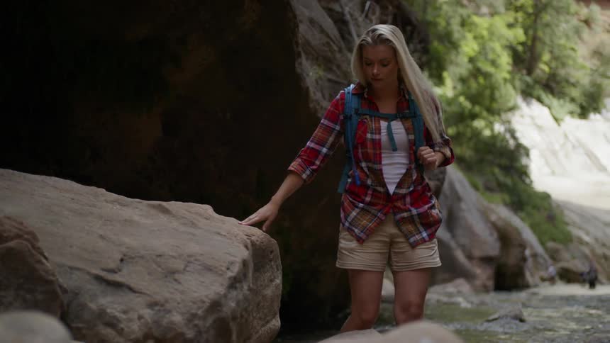Woman walking near a stream then sitting on a rock in the canyon