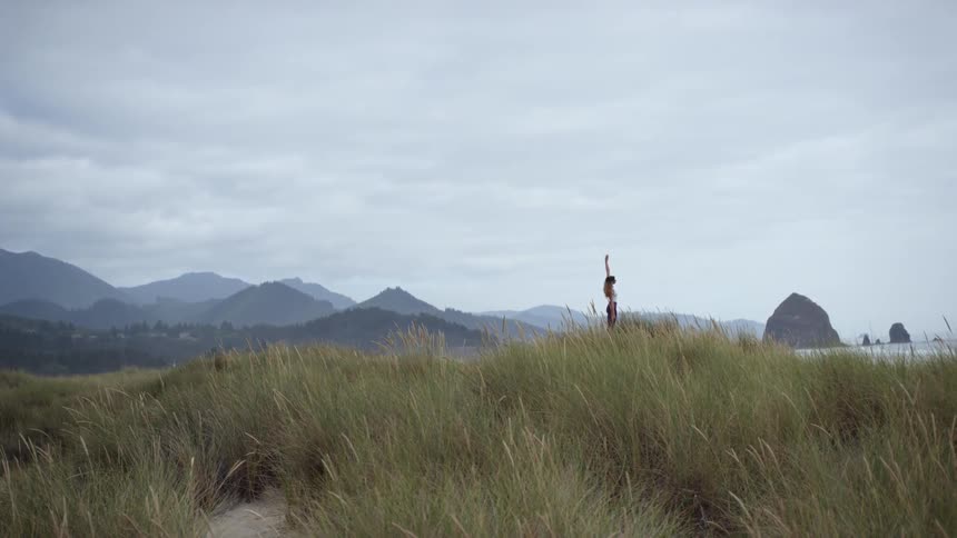 A woman stretches her arms up while standing on the beach