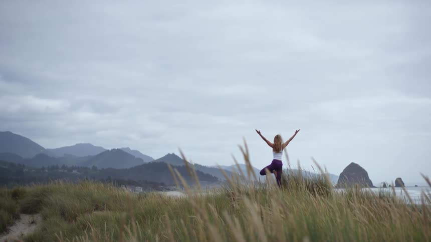 A white woman practices yoga near a beach