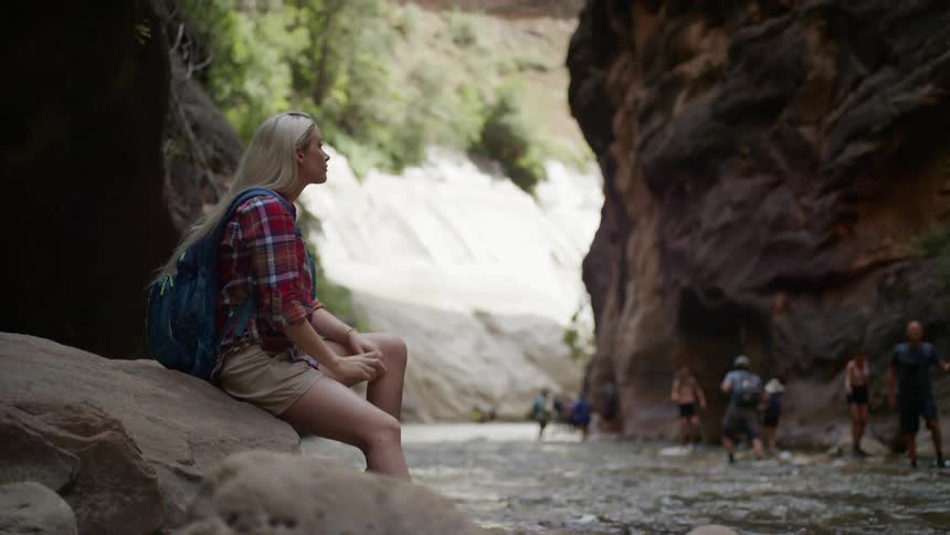 Blonde woman sitting on a rock looks around in the stream between two mountains