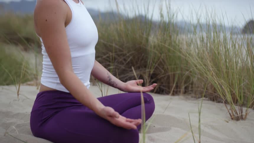 White woman practices yoga on the beach on a cloudy day