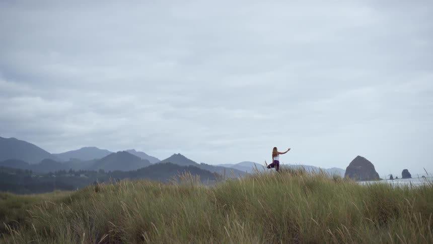 A woman does yoga outside surrounded by wild grasses and hills