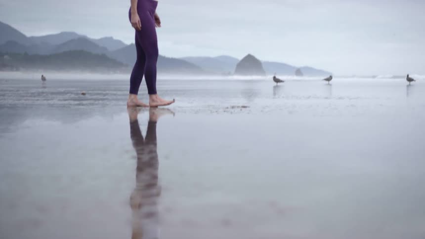 A woman stops on the beach and stretches her arms up