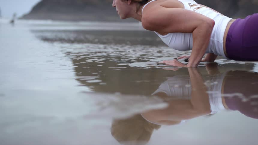 An athletic woman performs a yoga pose atop soggy wet sands on a beach