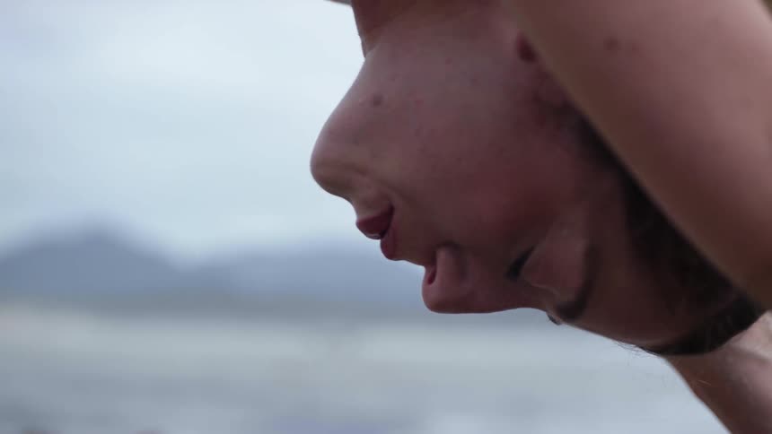 A woman closes her eyes as she does yoga on the beach