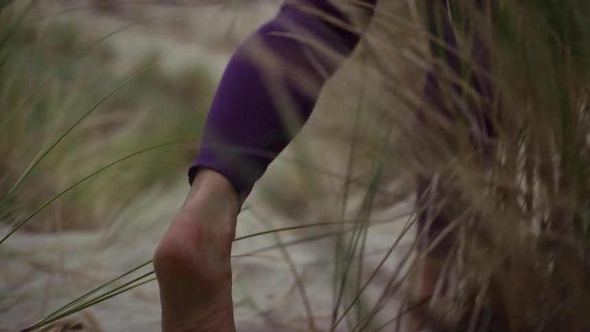 Woman wearing tights walks barefoot on the beach