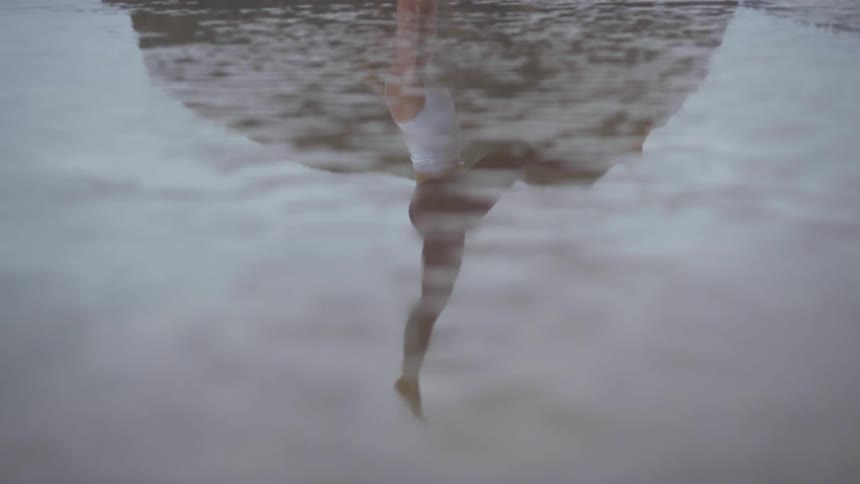 A woman does a hand stand in the sand on the beach