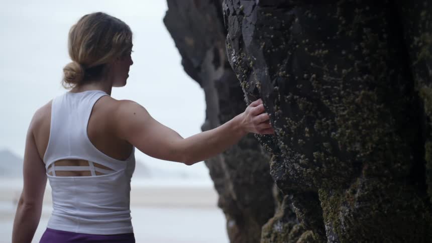 A woman touches rock as she walks by heading towards the beach