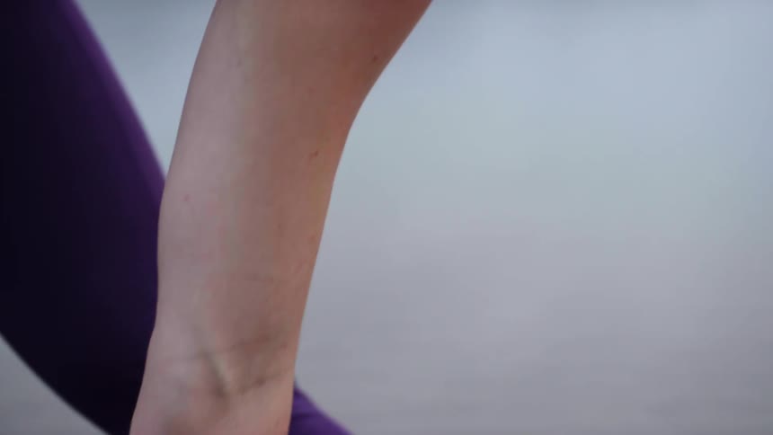 A woman reaches down and places her hand in the water on a beach while practicing yoga