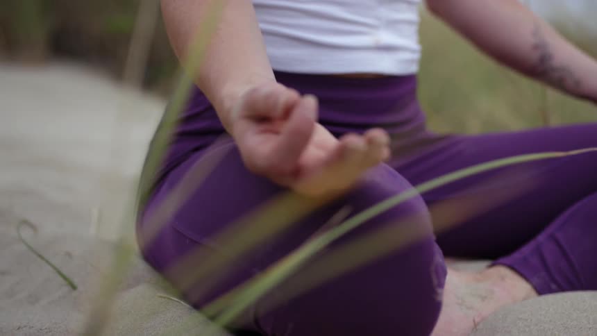 A woman sits cross legged and meditates on the beach